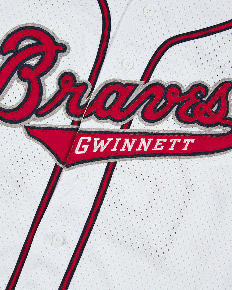 Close-up of the Ronald Acuña Jr. Gwinnett Braves Mesh Button-Up Jersey by Ebbets Field: a white jersey with red and black trim, Braves in bold script, and Gwinnett in smaller capitals underneath.