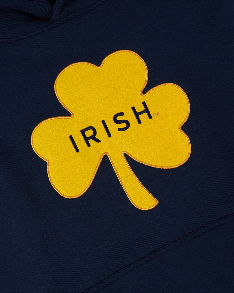 The Ebbets Field NOTRE DAME HOODIE NAVY features a yellow shamrock with IRISH in bold black letters, displayed on a dark blue fabric background.