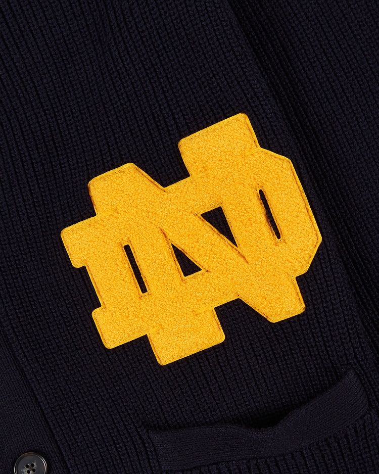 A close-up of the Ebbets Field NOTRE DAME VARSITY CARDIGAN Navy displays dark knit fabric with a prominent yellow ND monogram patch, representing the University of Notre Dame.