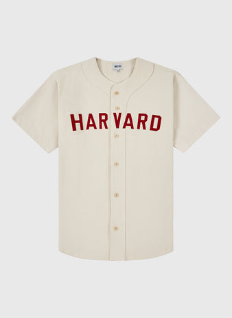 The Ebbets Field HARVARD COTTON TWILL JERSEY Natural is a cream-colored, short-sleeve button-up baseball jersey featuring bold red HARVARD lettering across the chest, shown on a plain white background.