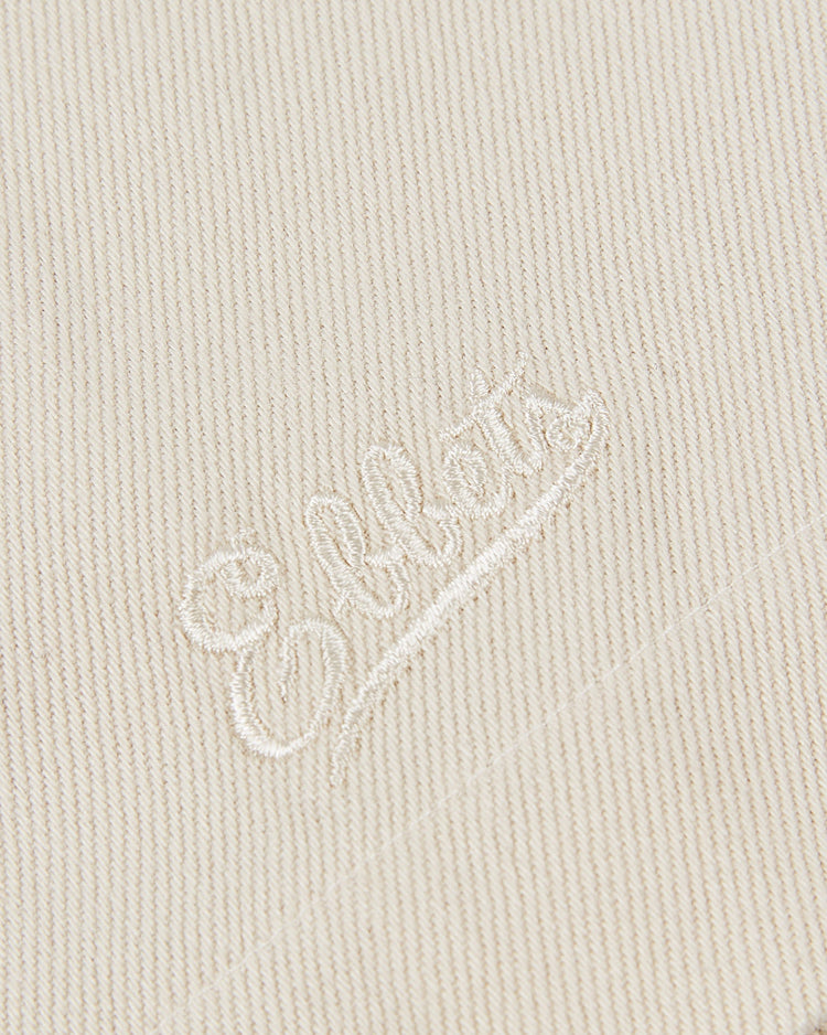 Close-up of Ebbets Field HARVARD COTTON TWILL JERSEY in Natural, showing cream-colored fabric with Elliott embroidered in matching thread and a visible textured weave.