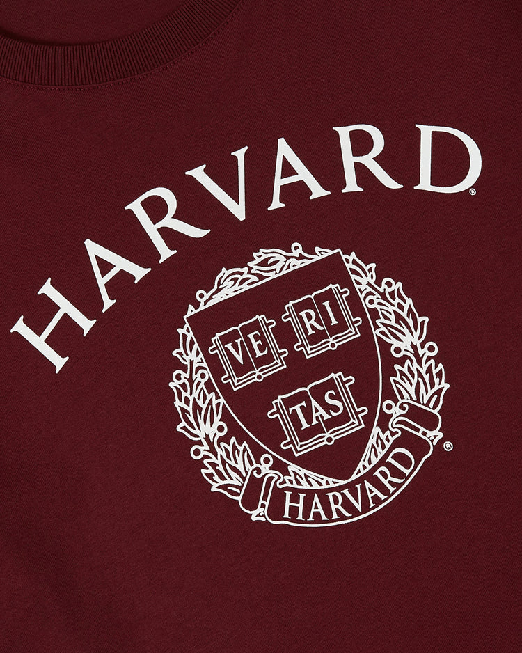 Close-up of the Ebbets Field HARVARD SS TEE MAR, a maroon t-shirt with the Harvard University logo and crest, showing HARVARD in bold white letters above a shield with VERITAS and laurel leaves.