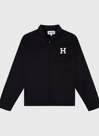The HARVARD GROUNDS CREW JACKET BLK by Ebbets Field is a black zip-up jacket with a collar, left chest pocket featuring a white H patch, and an inner collar tag reading HENRY PELLA.