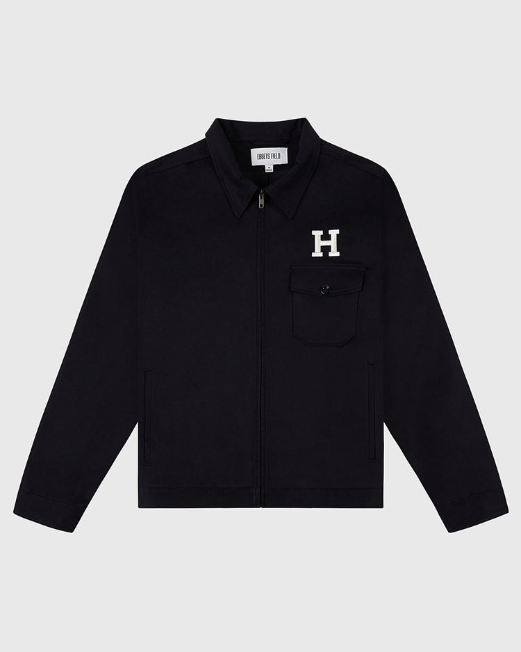 The HARVARD GROUNDS CREW JACKET BLK by Ebbets Field is a black zip-up jacket with a collar, left chest pocket featuring a white H patch, and an inner collar tag reading HENRY PELLA.