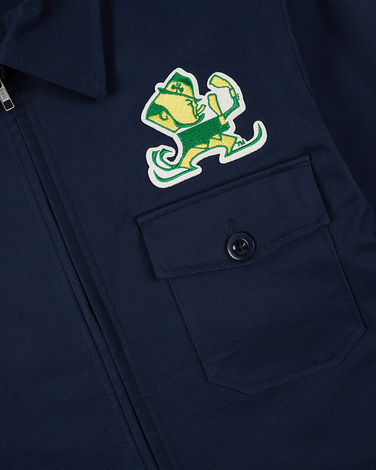 The Ebbets Field NOTRE DAME GROUNDS CREW JACKET in navy features a chest pocket with a button and an embroidered green and yellow fighting leprechaun mascot patch.