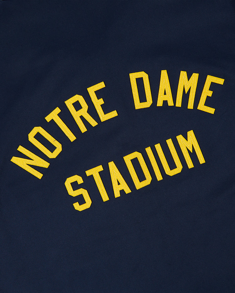 The Ebbets Field NOTRE DAME GROUNDS CREW JACKET in navy features large, arched yellow NOTRE DAME STADIUM lettering on the fabric.