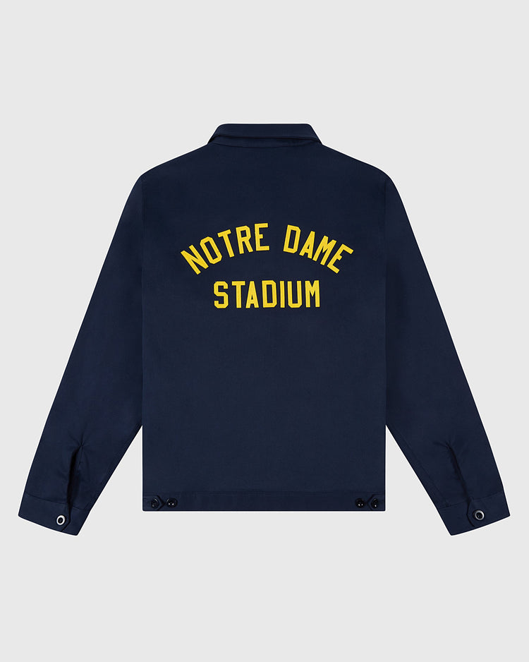 The NOTRE DAME GROUNDS CREW JACKET Navy by Ebbets Field features yellow NOTRE DAME STADIUM text on the back, with button details on the cuffs and waist.