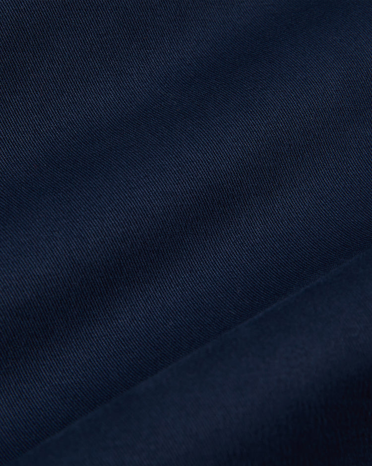 Close-up of the NOTRE DAME GROUNDS CREW JACKET in navy by Ebbets Field, featuring smooth, finely textured fabric with subtle diagonal lines and gentle folds that create soft shadows across its woven surface.