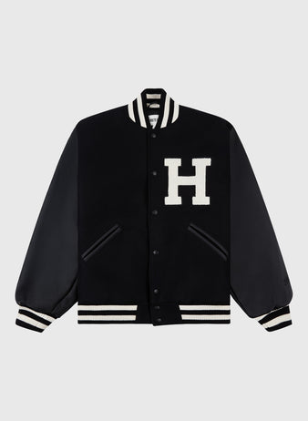 The Ebbets Field Harvard University Wool and Leather Varsity Jacket features black leather sleeves, white-striped ribbed trim, and a large white H on the chest—a modern take on the classic 1950s varsity style.