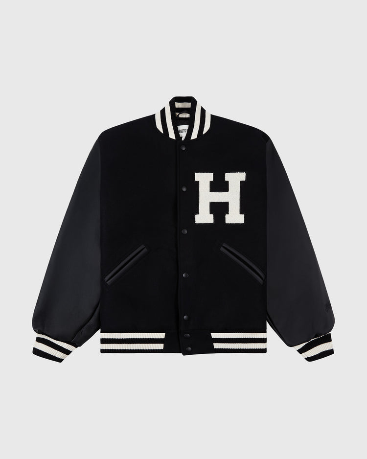 The HARVARD VARSITY JACKET BLK by Ebbets Field features black fabric, leather sleeves, striped ribbed cuffs and collar, front snap buttons, and a large white H patch on the left chest.