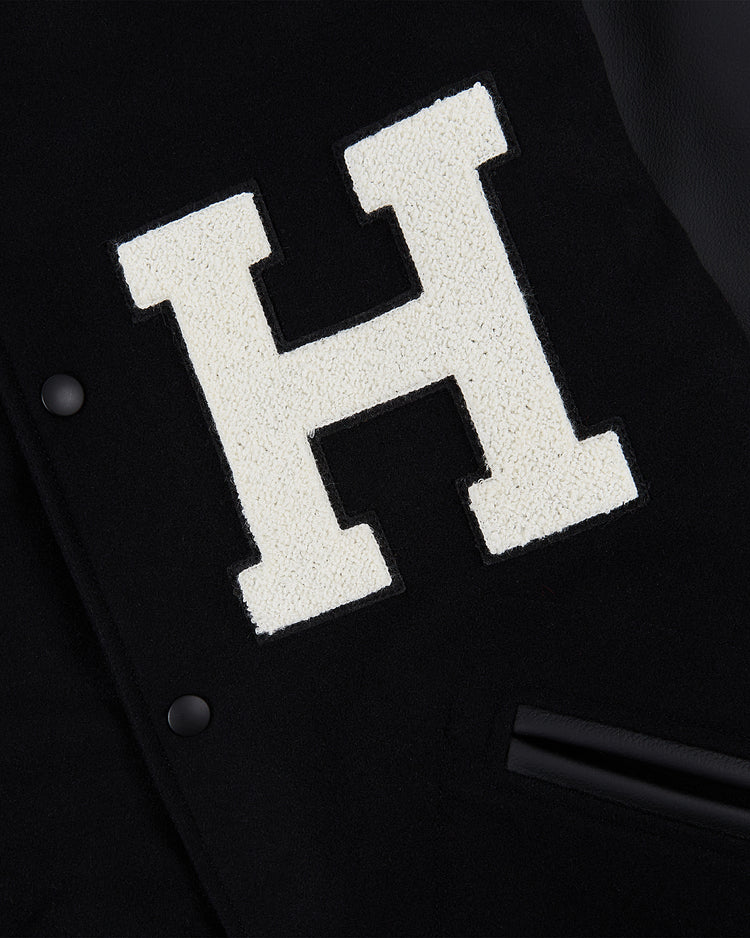 Close-up of the Ebbets Field Harvard University Wool and Leather Varsity Jacket, showcasing a large textured white H patch and black snap buttons in classic 1950s varsity style.