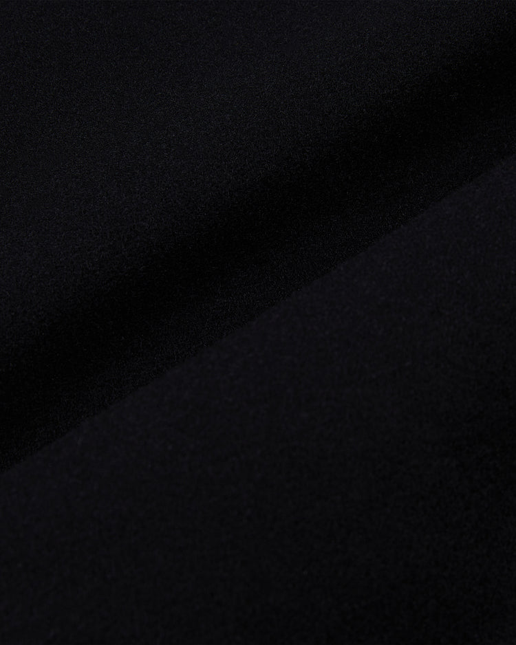 Close-up of the smooth black wool fabric from the Ebbets Field Harvard University Wool and Leather Varsity Jacket, showing a gentle diagonal fold across its textured surface.