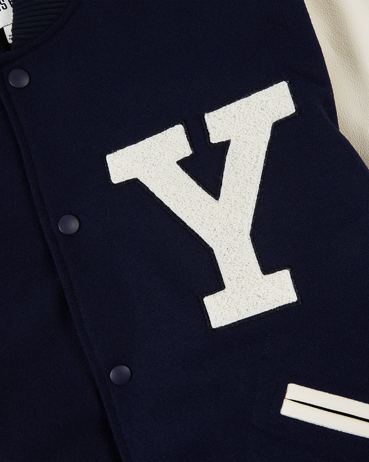 A close-up of the Ebbets Field YALE VARSITY JACKET in navy, showcasing a large white Y patch on the chest and a pocket detailed with two white stripes.
