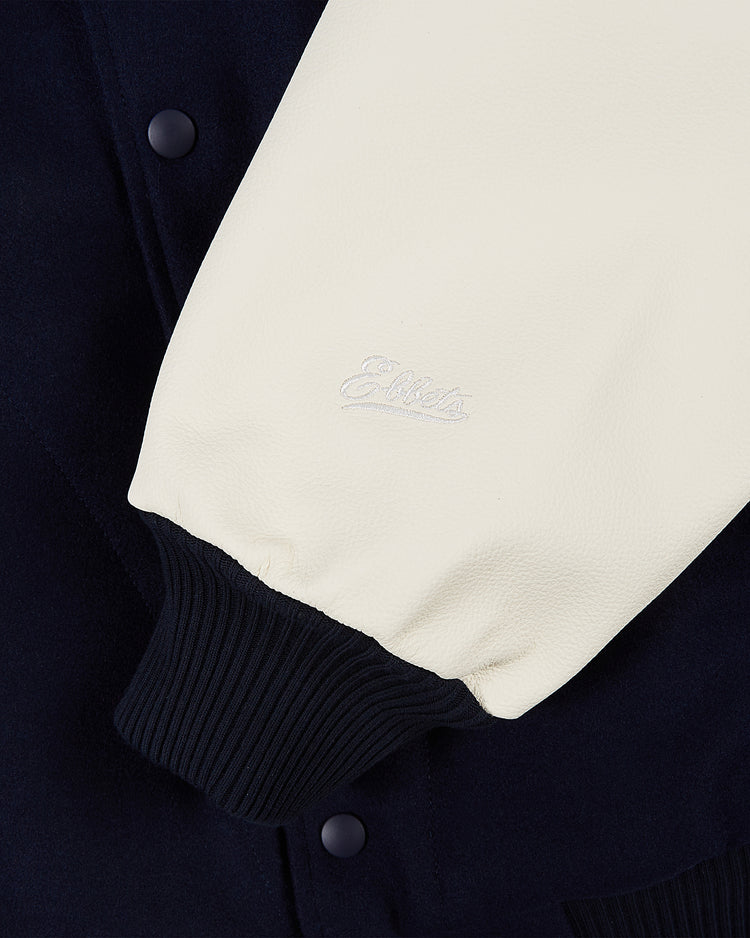 Close-up of the Ebbets Field YALE VARSITY JACKET Navy, featuring a cream leather sleeve with ribbed black cuff, embroidered text near the wrist, dark navy body, and black snap buttons.