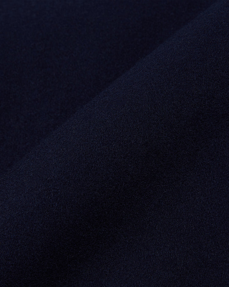 A close-up of the Ebbets Field YALE VARSITY JACKET in navy shows its soft, slightly fuzzy fabric. The material is folded diagonally, creating subtle shadows and a gradient effect across the surface.