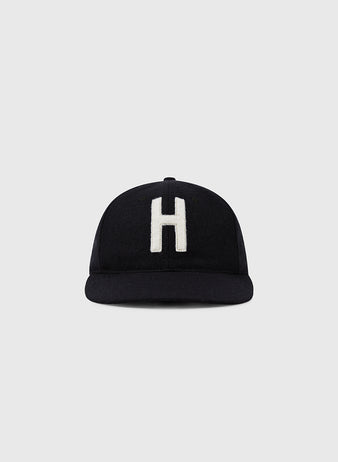 The Ebbets Field Harvard University 1950 Authentic Wool Ballcap is a black cap featuring a large white H on the front, inspired by the original Harvard ballcap, shown against a plain light gray background.