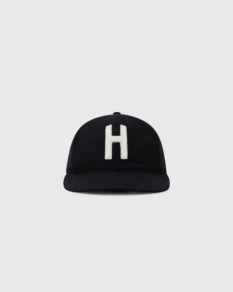 The Ebbets Field Harvard University 1950 Authentic Wool Ballcap is a black cap featuring a large white H on the front, inspired by the original Harvard ballcap, shown against a plain light gray background.
