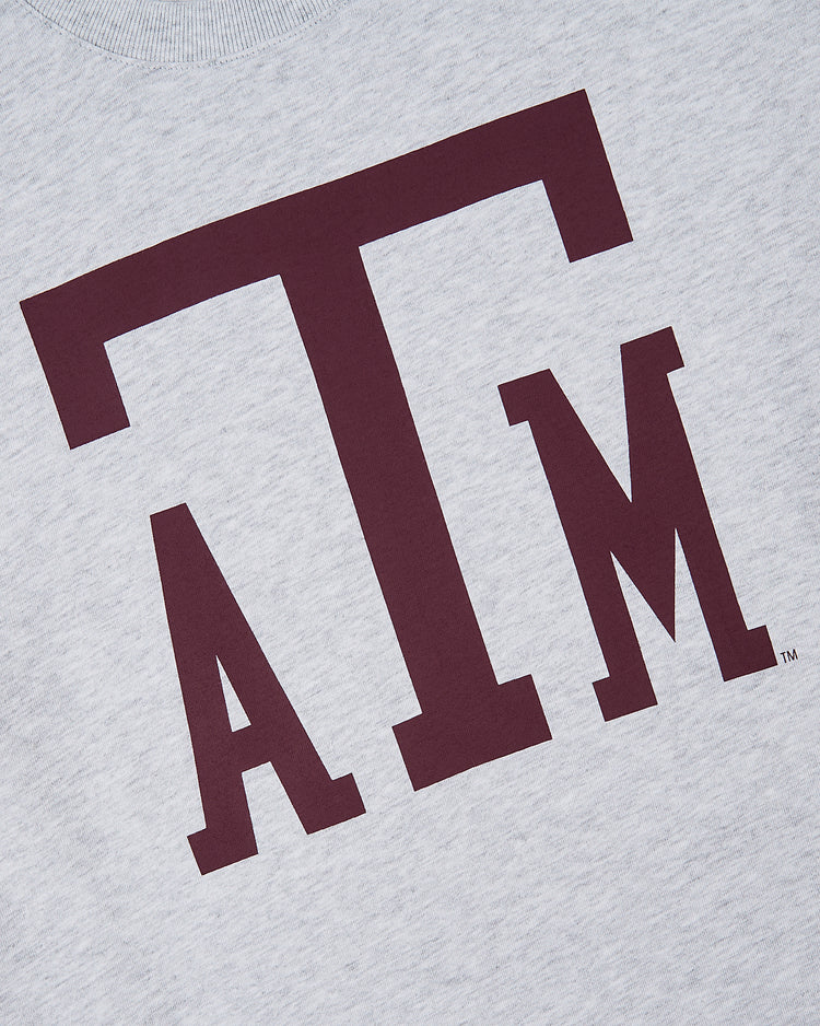 The Ebbets Field TEXAS A&M SS TEE H-GRY features large maroon ATM letters in a bold serif font on light gray fabric, representing the Texas A&M University logo.