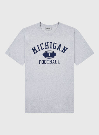 The Ebbets Field MICHIGAN SS TEE H-GRY is a light gray short-sleeve shirt featuring bold navy “MICHIGAN,” a football graphic with the number 1, and “FOOTBALL” below in navy text.