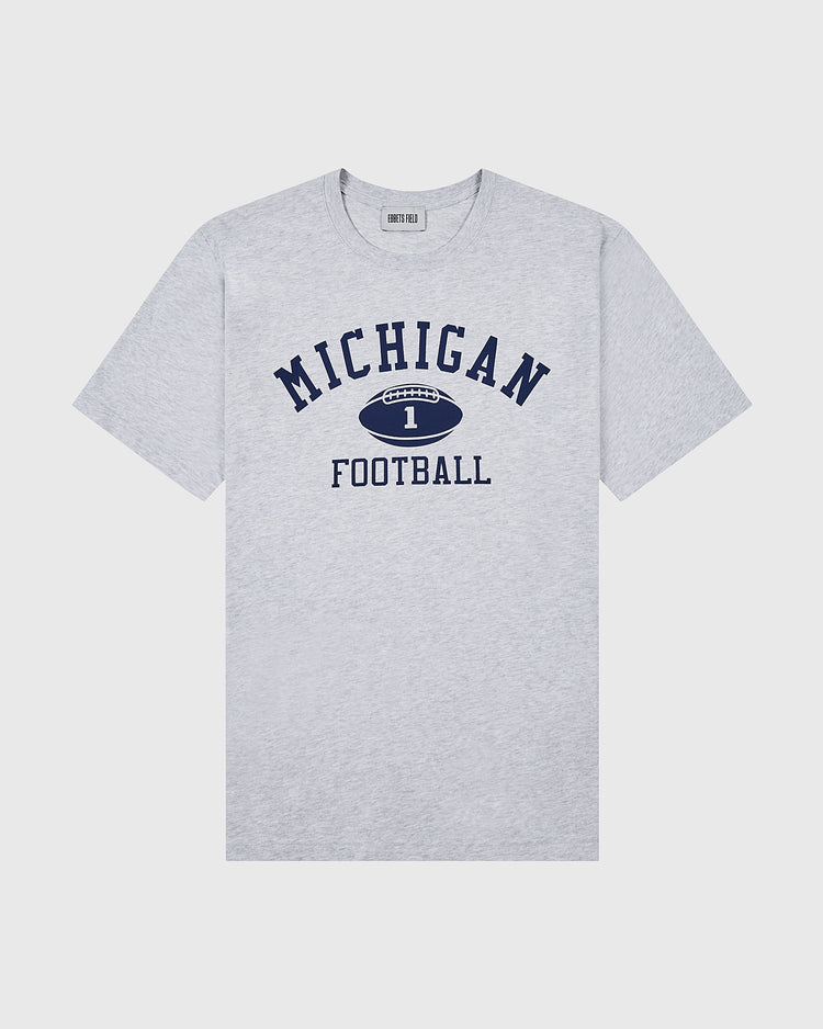 The Ebbets Field MICHIGAN SS TEE H-GRY is a light gray short-sleeve shirt featuring bold navy “MICHIGAN,” a football graphic with the number 1, and “FOOTBALL” below in navy text.