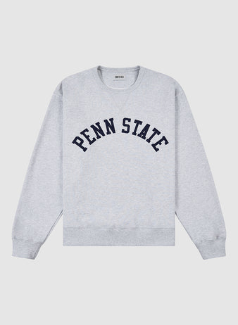 The PENN STATE CREWNECK SS H-GRY by Ebbets Field is a light gray sweatshirt featuring “PENN STATE” in bold navy block letters on the chest, with ribbed cuffs, collar, and hem.