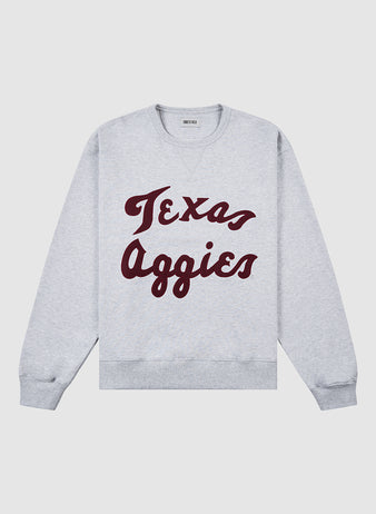 The Ebbets Field TEXAS A&M CREWNECK SS H-GRY is a light gray crewneck sweatshirt featuring bold maroon Texas Aggies script across the front.