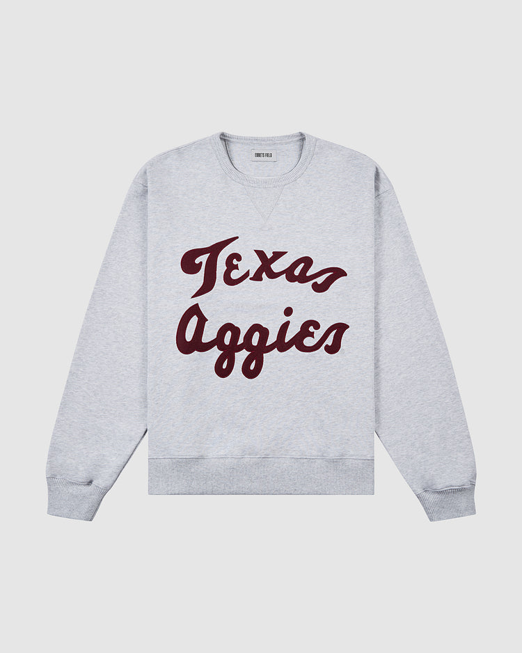 The Ebbets Field TEXAS A&M CREWNECK SS H-GRY is a light gray crewneck sweatshirt featuring bold maroon Texas Aggies script across the front.