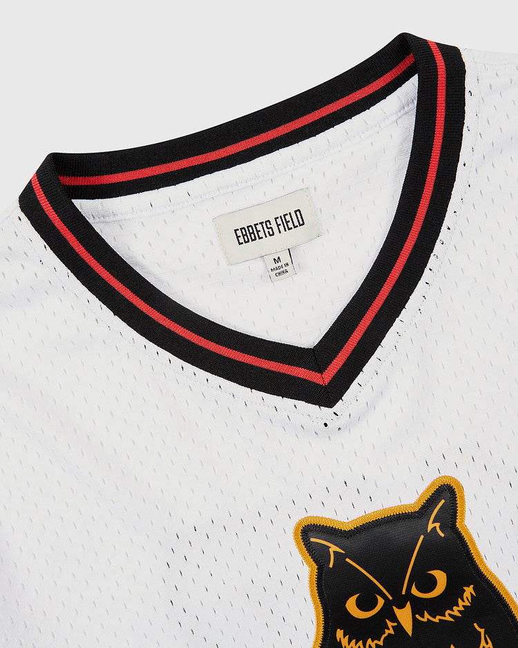 Close-up of the Topeka Owls V-Neck Mesh Jersey by Ebbets Field, featuring a white mesh fabric, black and red striped V-neck collar, EBBETS FIELD tag, and part of the yellow and black Topeka Owls team graphic on the chest.