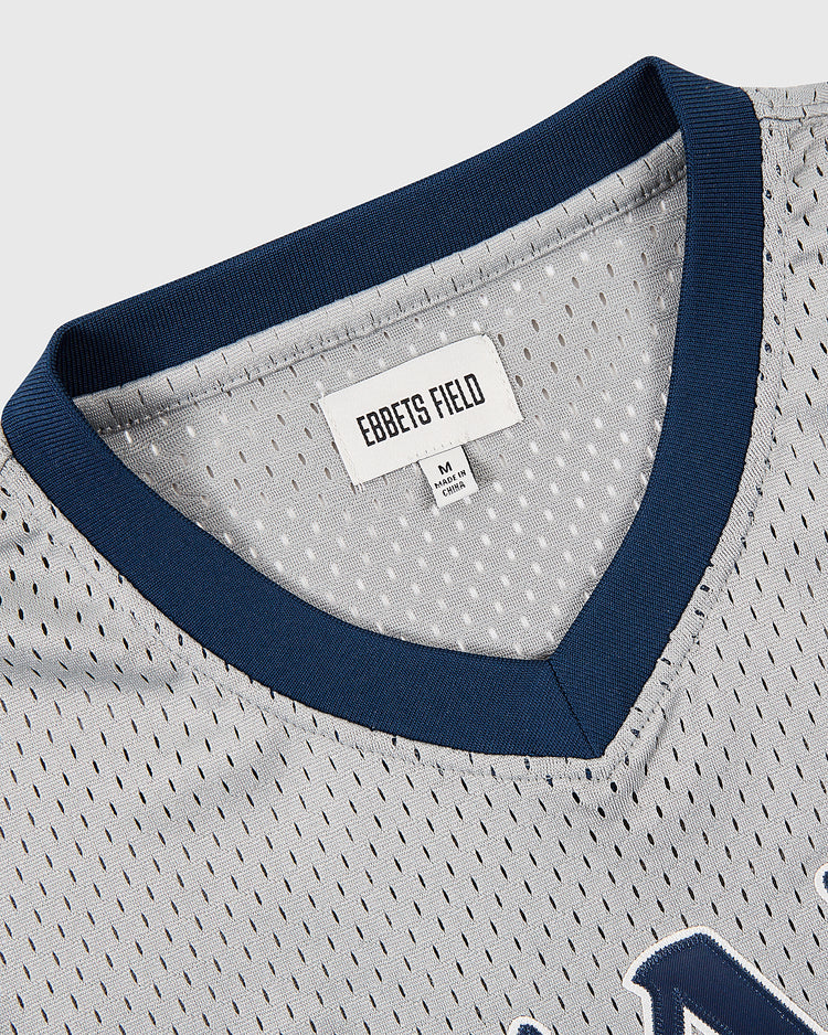 Close-up of the collar and neckline of the Osaka Tigers Mesh V-Neck Jersey by Ebbets Field, featuring light gray mesh with navy trim in classic Japanese baseball style. Inside, a white Ebbets Field tag appears above a size M label.