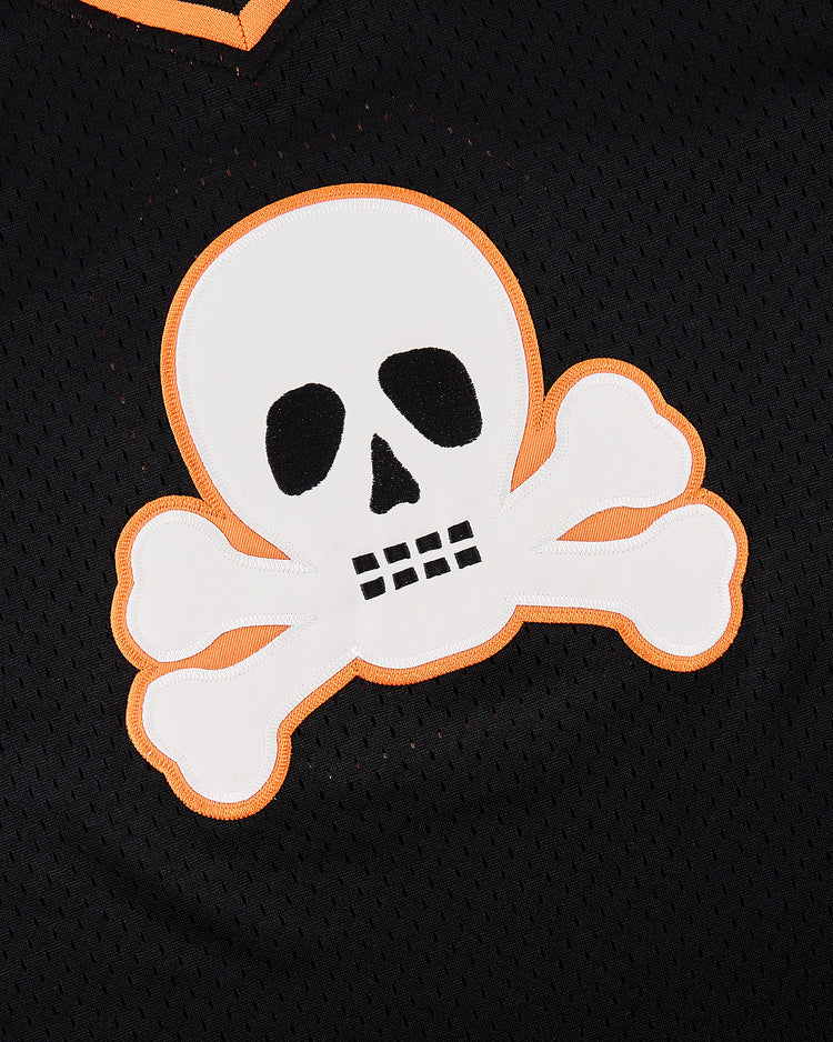 A white skull and crossbones with an orange outline appears on black perforated fabric, featured on the Ebbets Field Sioux City Ghosts Mesh V-Neck Jersey.