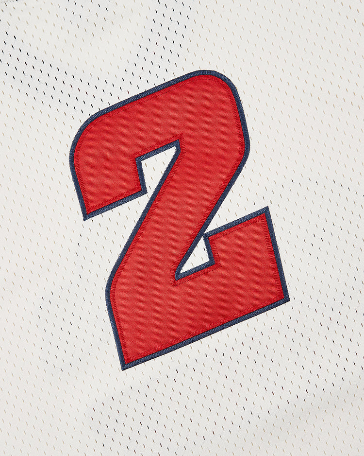 A large red number 2 with a blue outline is stitched onto white mesh fabric, recalling classic Atoms Boy uniforms in the Sankei Atoms Mesh V-Neck Jersey by Ebbets Field.