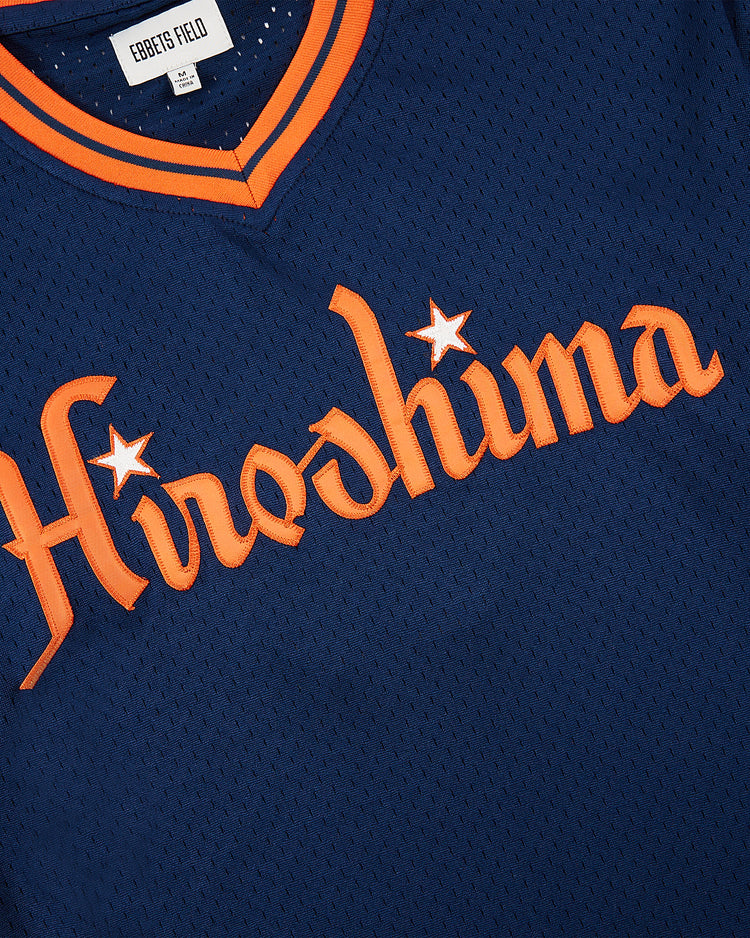 The Ebbets Field Hiroshima Carp Mesh V-Neck Jersey features dark blue mesh, orange trim, “Hiroshima” in stylized orange letters with star accents, and a nod to Japanese baseball with an Ebbets Field collar label.