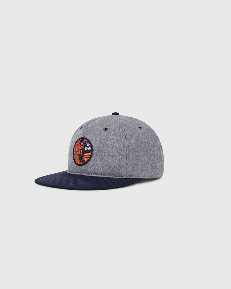 The Ebbets Field Hiroshima Carp Cotton Twill Ballcap features a gray crown, dark blue brim, and a round orange-black patch—ideal for Hiroshima Carp fans. Displayed on a light gray background.