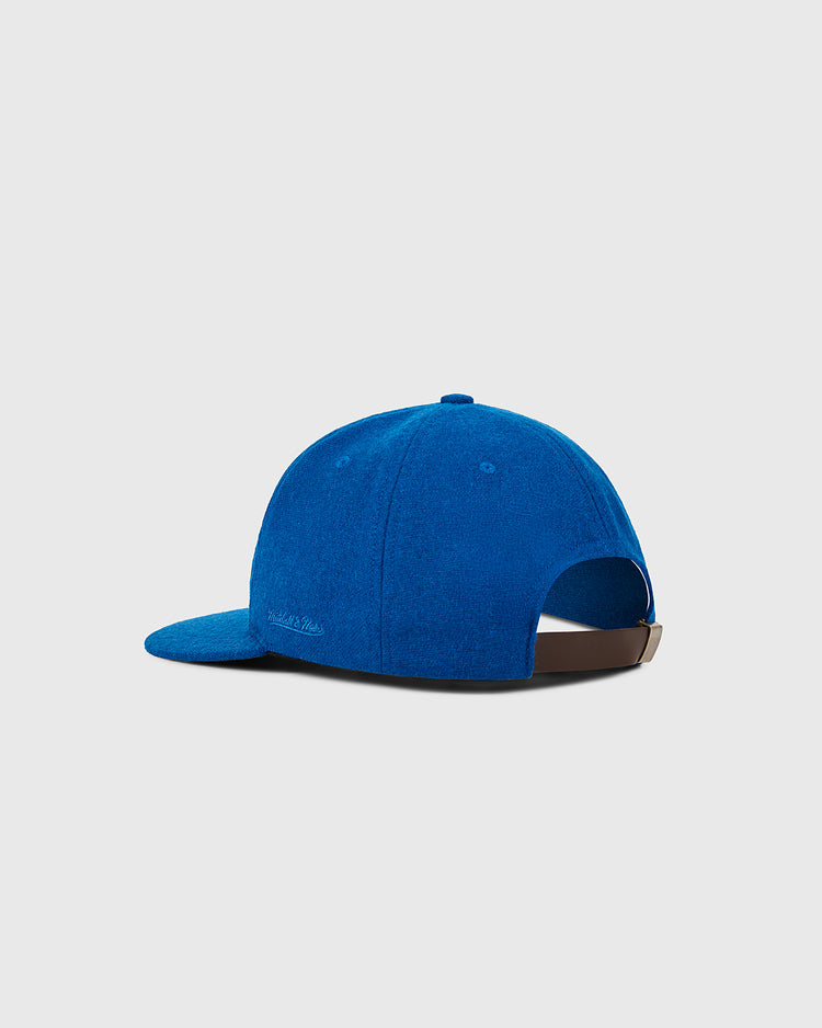 A royal blue New York Mets 1962 MLB Authentic Wool Ballcap by Ebbets Field, seen from the back, with a curved brim and an adjustable brown strap with metal buckle. The background is plain light gray.