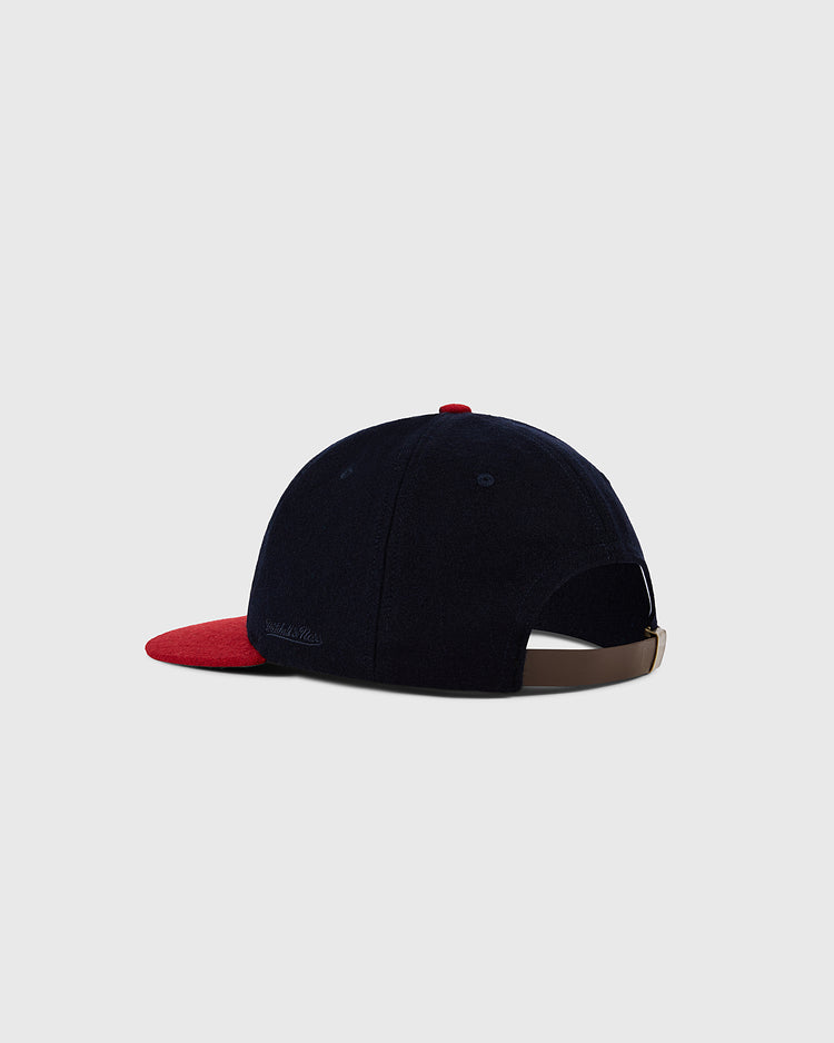 The Ebbets Field Milwaukee Braves 1953 MLB Authentic Wool Ballcap, navy with a red brim and top button, is shown from the back. It features a brown adjustable strap with metal buckle, part of the Decade of Change Collection on a light gray background.