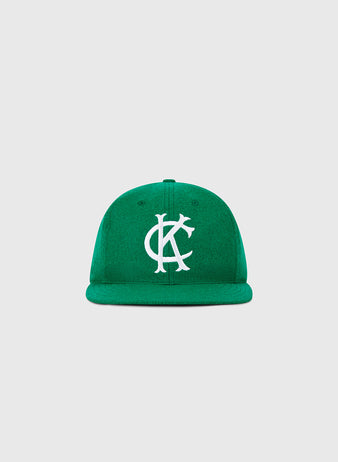 The Ebbets Field Kansas City Athletics 1963 MLB Authentic Wool Ballcap features a green flat brim and large white interlocking KC embroidery, inspired by the Decade of Change Collection. Shown on a plain light gray background.