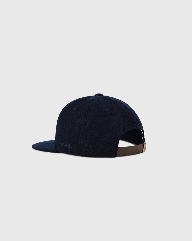 A dark blue Cleveland Indians 1958-1961 MLB Authentic Wool Ballcap by Ebbets Field, shown from the back left with a brown adjustable strap and metallic clasp, set on a plain light gray background. Part of the Decade of Change Collection.
