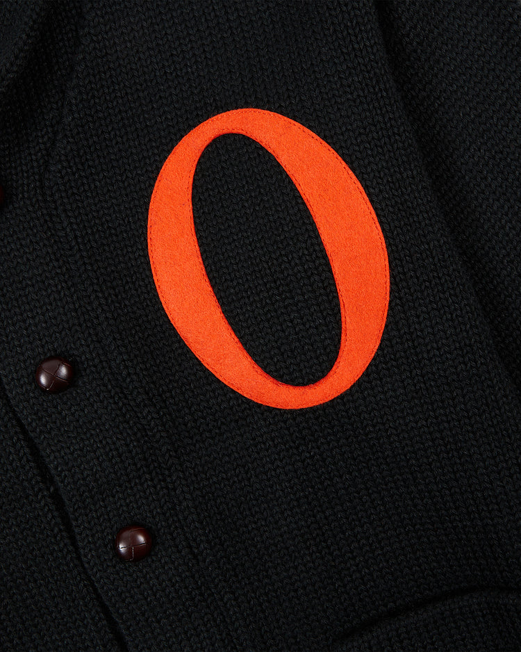 Close-up of the EFF Baltimore Orioles 1901 Wool Shawl Collar Sweater, featuring black textured fabric, brown buttons, and a bold orange “O” appliqué inspired by the original 1901 design.