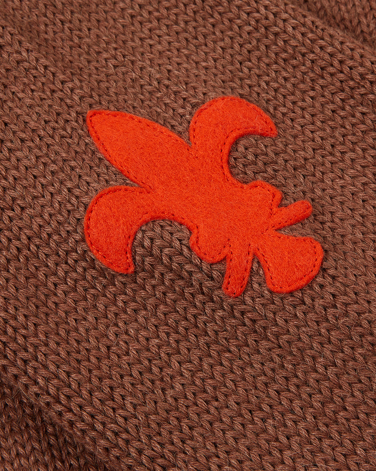 A close-up of the EFF St. Louis Browns 1909 Wool Cardigan Sweater shows its brown knit fabric with an orange fleur-de-lis patch, inspired by vintage styles worn by legends like Rube Waddell.