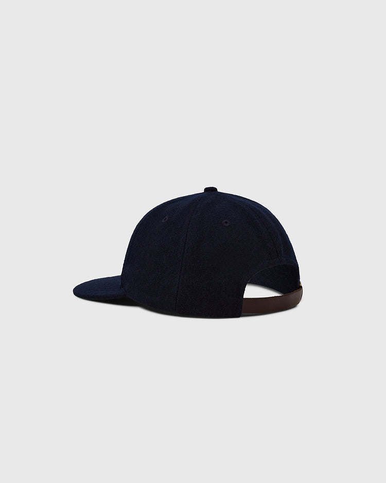 A Darby Daisies 1932 Authentic Wool Ballcap by EFF, in dark blue, is shown from the back and side on a light gray background, with a curved brim and an adjustable brown strap at the back.