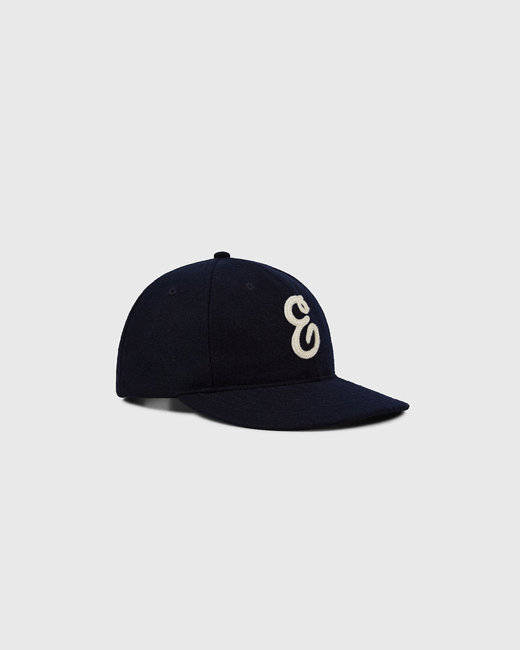 The Ebbets Felt 'E' Wool Ballcap by Ebbets Field is a navy wool vintage cap with a white embroidered “E” on the front, shown against a light gray background.
