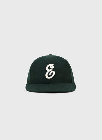 The Ebbets Felt 'E' Wool Ballcap by Ebbets Field is a dark green vintage-style wool cap, featuring a white embroidered “E” on the front, shown against a plain light gray background.