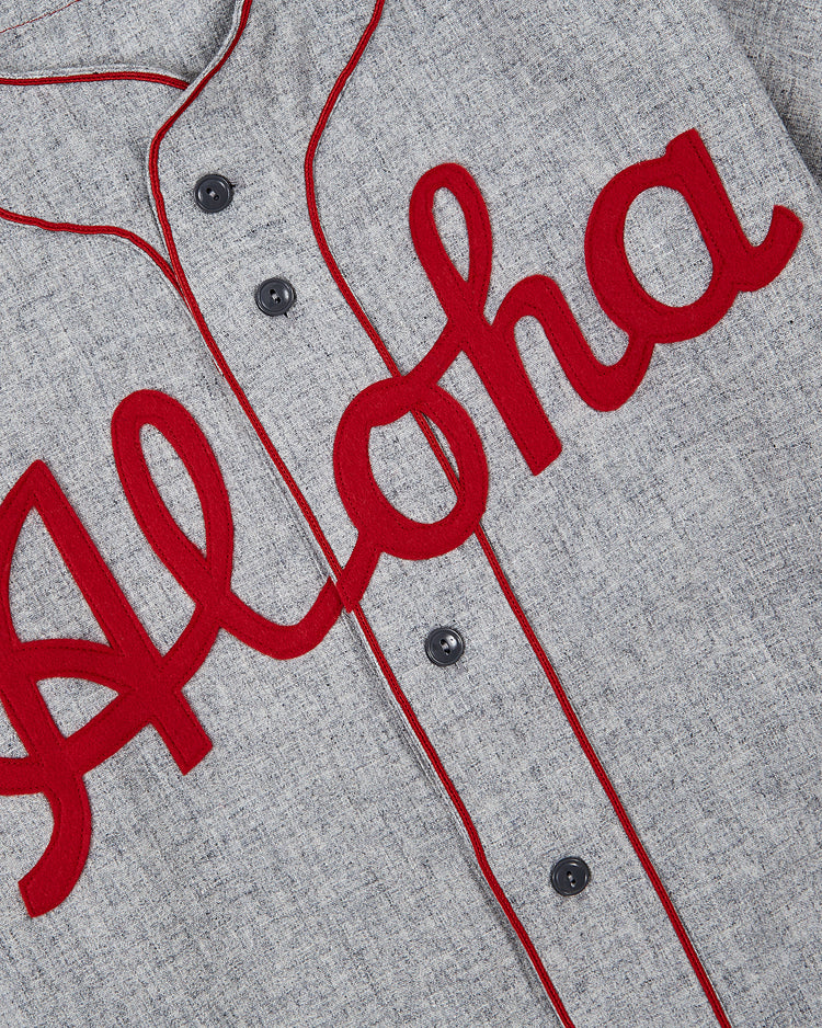 A close-up of the Ebbets Field Aloha 100th Infantry 1942 Authentic Wool Road Baseball Jersey, a gray button-up with red piping and 