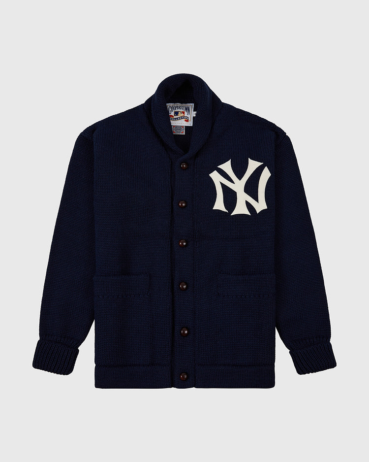 The Ebbets Field New York Yankees 1922 Wool Shawl Collar Sweater is navy blue with two front pockets, a large white NY logo on the left chest, and features a ribbed collar, cuffs, and hem for classic comfort.