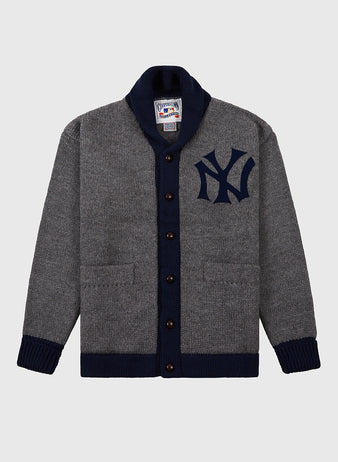 The Ebbets Field New York Yankees 1922 Wool Shawl Collar Sweater is a gray button-up with a dark blue collar, cuffs, hem, Yankees chest logo, and two front pockets, inspired by the team’s authentic 1922 sweater.