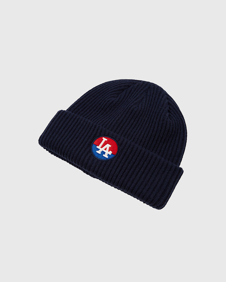 The Ebbets Field Los Angeles Angels (PCL) Patch Logo Ribbed Beanie is a navy blue knit hat with a folded brim, featuring a round patch of the embroidered LA logo on a red and blue background at the front.