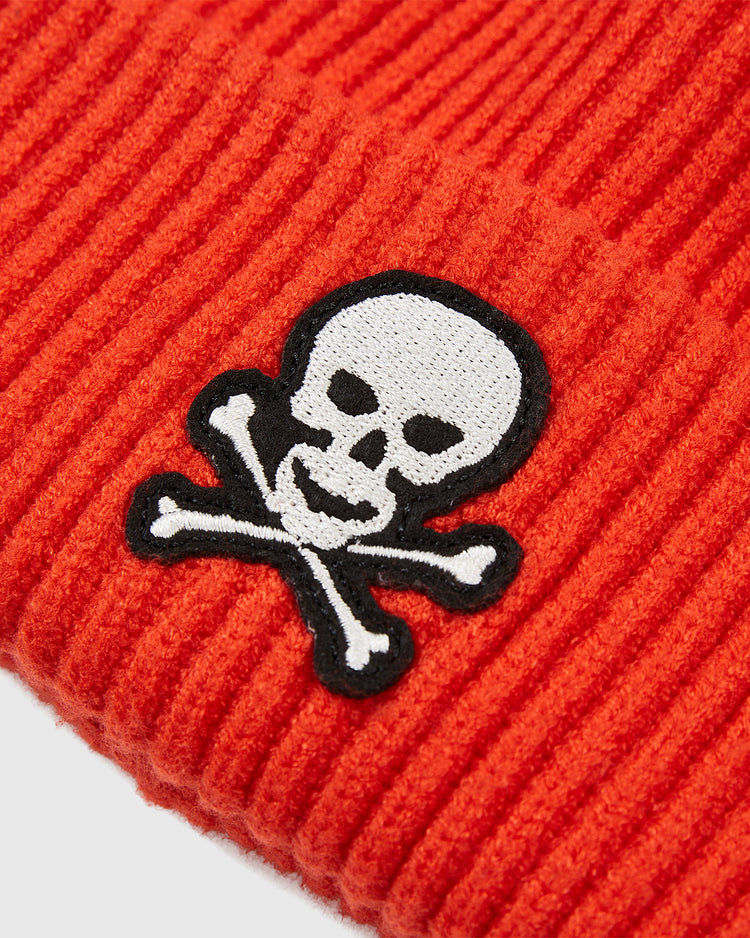 A close-up of the Sioux City Ghosts Embroidered Felt Ribbed Beanie by Ebbets Field shows its orange knit and white skull-and-crossbones patch—ideal for fast-pitch softball fans or Sioux City Ghosts supporters.