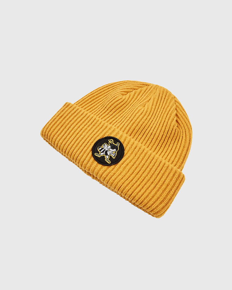 The Ebbets Field Salt Lake Bees Patch Logo Ribbed Beanie features a mustard yellow ribbed knit with a folded brim and a round black patch displaying the stylized white and yellow team logo, shown on a plain white background.
