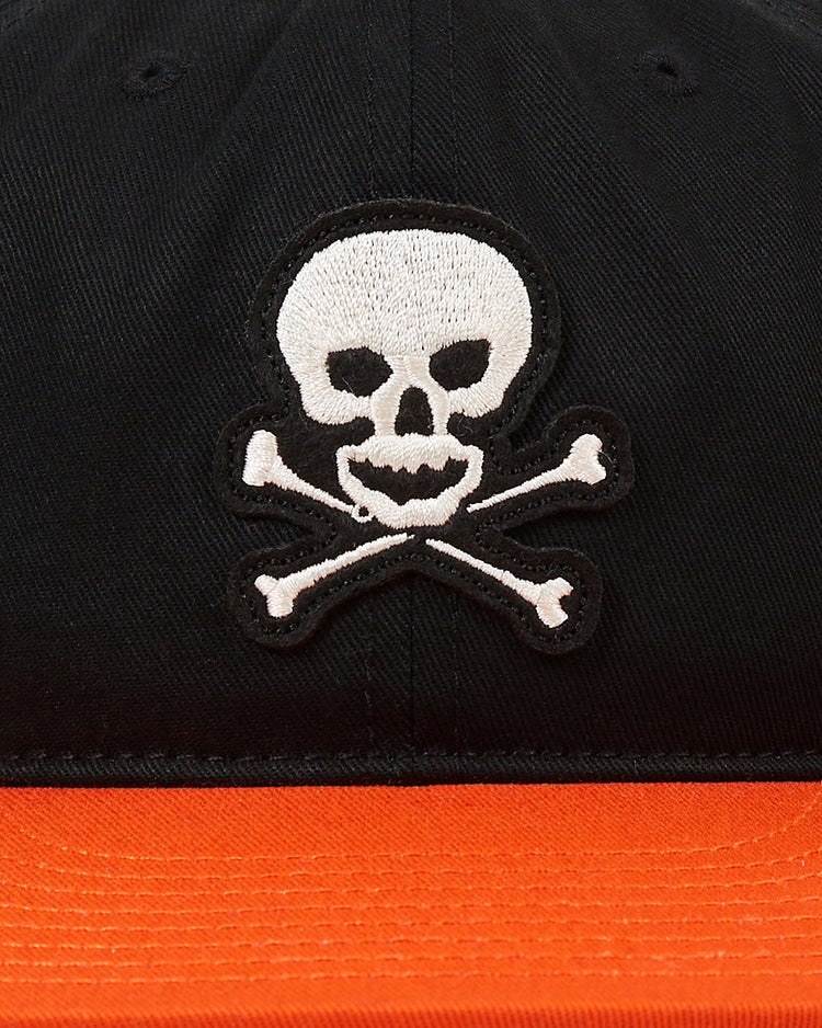 A close-up of the Sioux City Ghosts Cotton Twill Ballcap by Ebbets Field, featuring a white skull and crossbones embroidered on the front and an orange brim, inspired by the historic softball team.