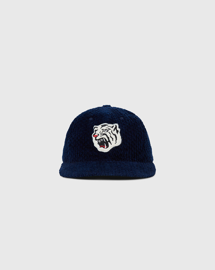 The Osaka Tigers Japanese Indigo Corduroy Ballcap by Ebbets Field features indigo-dyed corduroy and a white tiger head with open mouth and red tongue, inspired by the Osaka Tigers, on a light gray background.